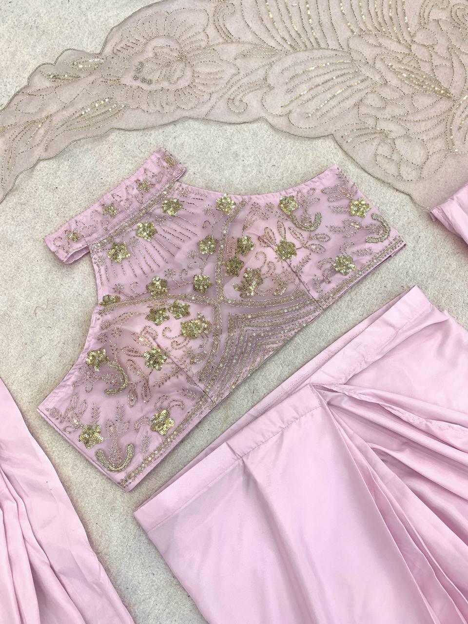 A light pink traditional outfit featuring an embroidered blouse top with gold and silver beadwork and matching pleated pink pants.
