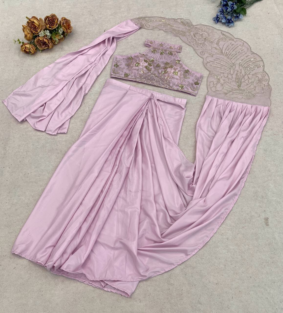 A light pink traditional outfit featuring a draped skirt, a matching sleeveless top with floral embroidery, and a sheer lace dupatta
